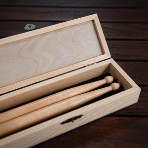 May include: A wooden box with a hinged lid, open to reveal two wooden drumsticks inside.