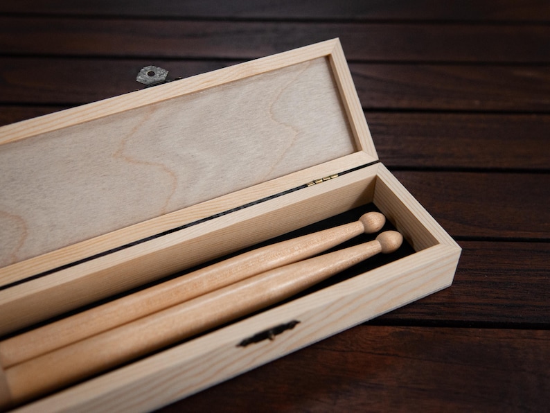 May include: A wooden box with a hinged lid, open to reveal two wooden drumsticks inside.