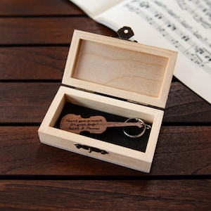 Puede incluir: Una caja de madera con un llavero en forma de viol&iacute;n en su interior. El llavero est&aacute; grabado con el texto "Muchas gracias por tu ayuda! Sarah & Thomas".