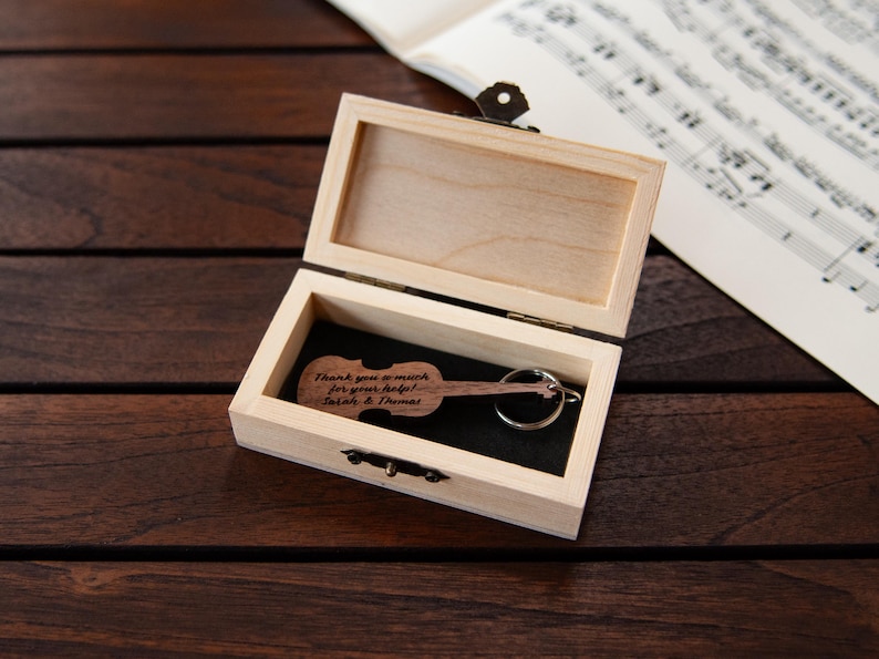 Puede incluir: Una caja de madera con un llavero en forma de viol&iacute;n en su interior. El llavero est&aacute; grabado con el texto "Muchas gracias por tu ayuda! Sarah & Thomas".