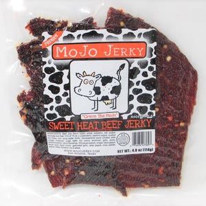 May include: A bag of Mojo Jerky Sweet Heat Beef Jerky, featuring a cartoon cow with the text "Crave The Mojo" and a black and white cow print background. The bag contains 4 ounces (114 grams) of jerky.