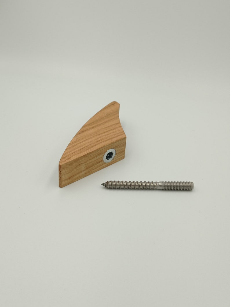 May include: A wooden furniture component with a curved shape, featuring a hexagonal bolt and a separate metal screw. The wood has a natural grain and light brown color. The screw is silver.
