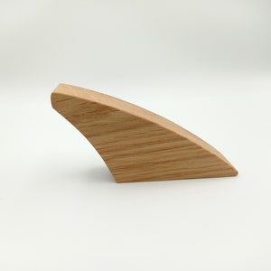 May include: A single, curved wooden object with a light brown color and visible wood grain. The object has a smooth, rounded top and a curved, angled base. The design is minimalist and modern, suggesting a decorative or functional item.