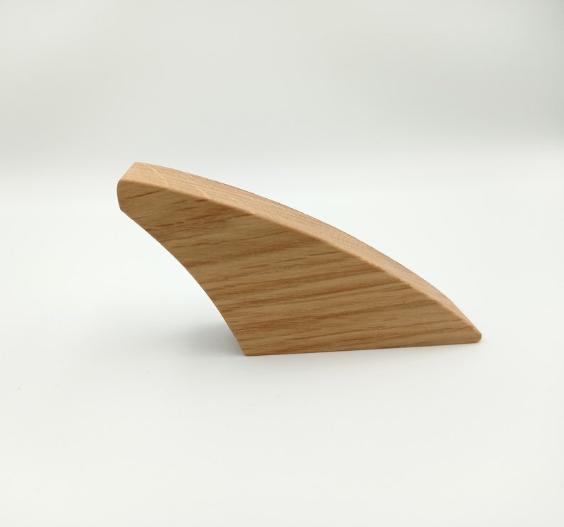 May include: A single, curved wooden object with a light brown color and visible wood grain. The object has a smooth, rounded top and a curved, angled base. The design is minimalist and modern, suggesting a decorative or functional item.