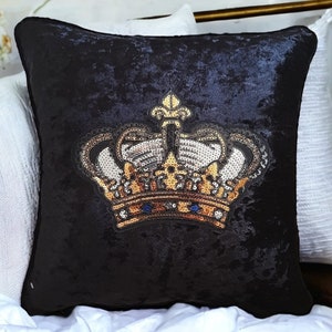 May include: Black velvet cushion featuring a gold and silver sequined crown design.
