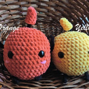 Peut inclure: Deux jouets en peluche crochet&eacute;s dans un panier en osier. Le jouet orange a un petit chapeau pointu et le jouet jaune a un chapeau arrondi. Les deux jouets ont des yeux noirs et des joues roses.