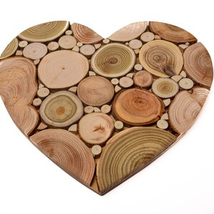 May include: A heart-shaped wooden wall decor made of many small, round wood slices. The wood slices are arranged in a pattern and have a natural wood color.