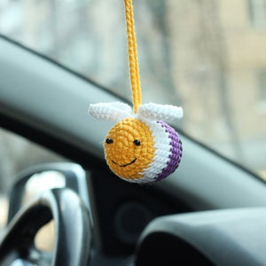 May include: A crocheted bee car charm with yellow, white, and purple stripes hanging from a rearview mirror.