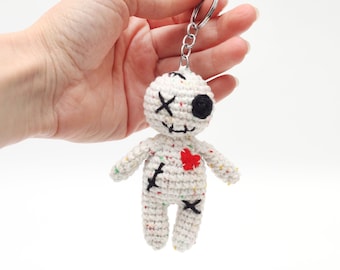 May include: White crocheted voodoo doll keychain with black eyes, a red heart, and stitched details.