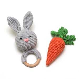 May include: A gray crocheted bunny rattle with a wooden ring and an orange crocheted carrot with green leaves.