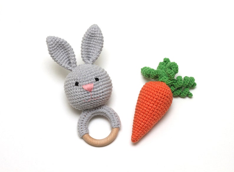 May include: A gray crocheted bunny rattle with a wooden ring and an orange crocheted carrot with green leaves.