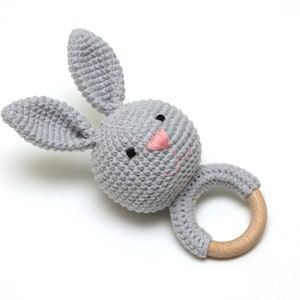 May include: A gray crocheted bunny rattle with a wooden ring. The bunny has a pink nose and black eyes.