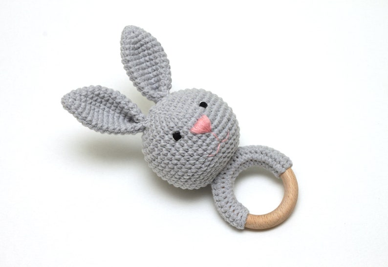 May include: A gray crocheted bunny rattle with a wooden ring. The bunny has a pink nose and black eyes.