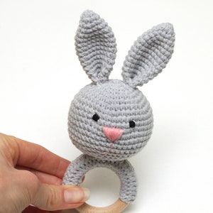 May include: A gray crocheted bunny rattle with a wooden ring. The bunny has black eyes and a pink nose.