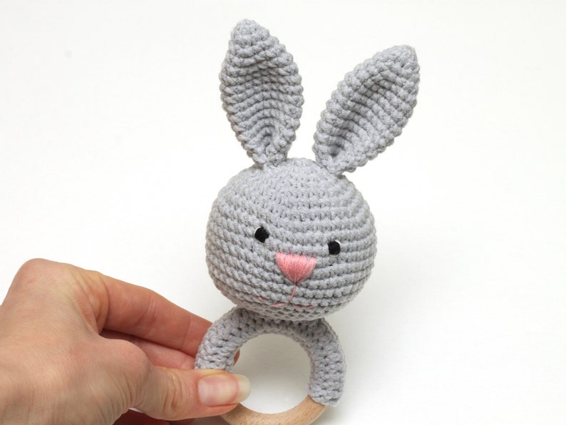 May include: A gray crocheted bunny rattle with a wooden ring. The bunny has black eyes and a pink nose.