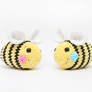 May include: Two crocheted bee plushies, one with pink cheeks and one with blue cheeks. The bees are yellow and black with white wings.