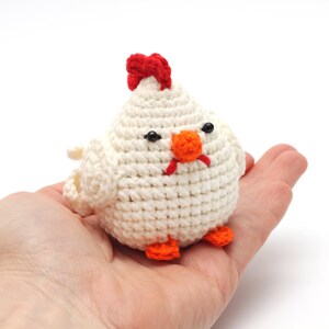 K&ouml;nnte beinhalten: Ein wei&szlig;es H&auml;keltier in Form eines Huhns mit rotem Kamm, orangem Schnabel und schwarzen Augen. Das Huhn sitzt in der Handfl&auml;che.