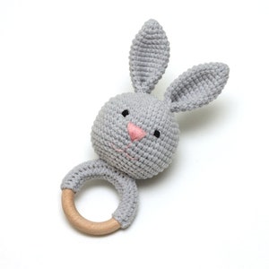 May include: A gray crocheted bunny rattle with a wooden ring. The bunny has pink embroidered nose and black eyes.