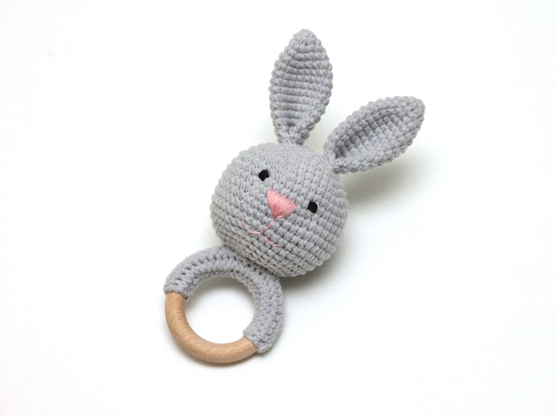May include: A gray crocheted bunny rattle with a wooden ring. The bunny has pink embroidered nose and black eyes.