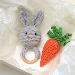 May include: A gray crocheted bunny rattle with a wooden ring and a crocheted orange carrot with green leaves.
