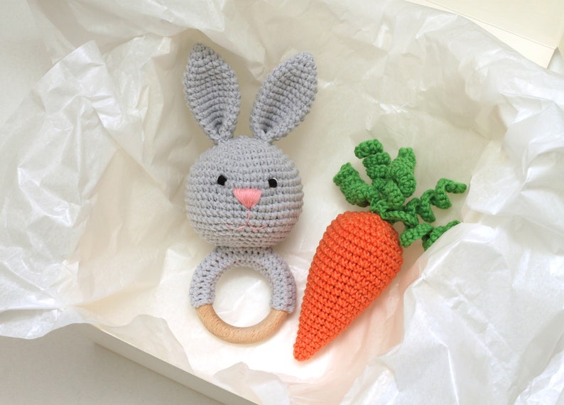 May include: A gray crocheted bunny rattle with a wooden ring and a crocheted orange carrot with green leaves.