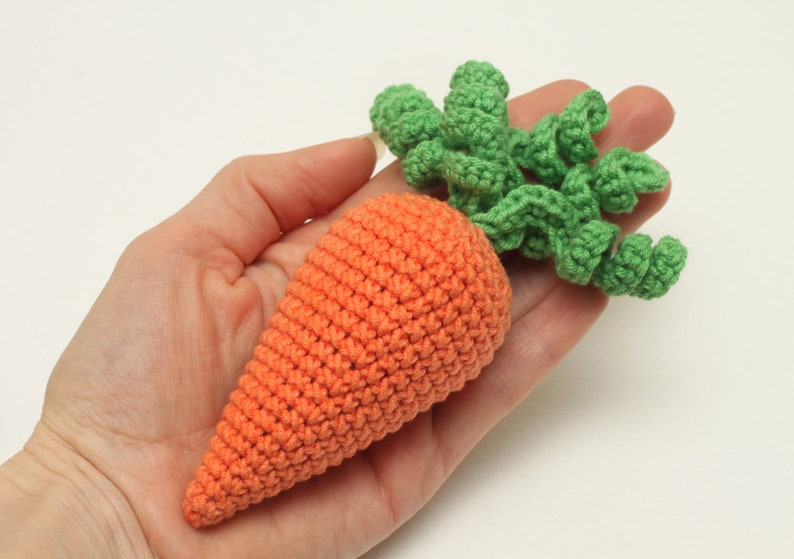 May include: A crocheted carrot toy with a green leafy top. The carrot is orange and the leaves are green.