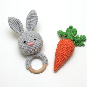 May include: A gray crocheted bunny rattle with a wooden ring and a crocheted orange carrot with green leaves.
