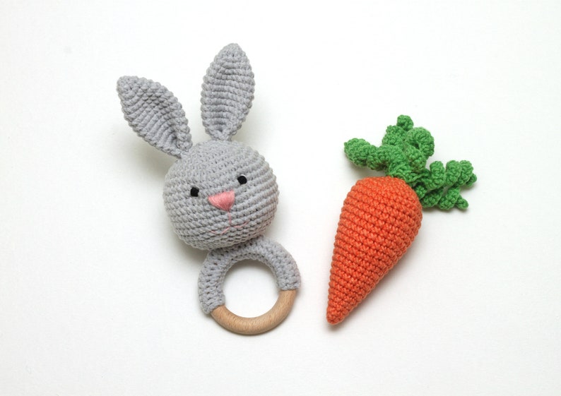 May include: A gray crocheted bunny rattle with a wooden ring and a crocheted orange carrot with green leaves.