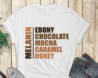 May include: White t-shirt with the word "MELANIN" in brown text on the left side and the words "EBONY", "CHOCOLATE", "MOCHA", "CARAMEL", and "HONEY" in brown text on the right side.