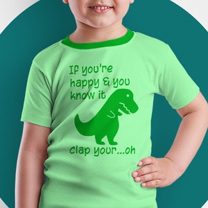 May include: A light green t-shirt with a green dinosaur graphic and the text "If you're happy & you know it clap your...oh".
