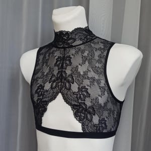 Pode incluir: Top preto de renda com al&ccedil;as, gola alta e um decote na frente. O top &eacute; feito de renda floral delicada.