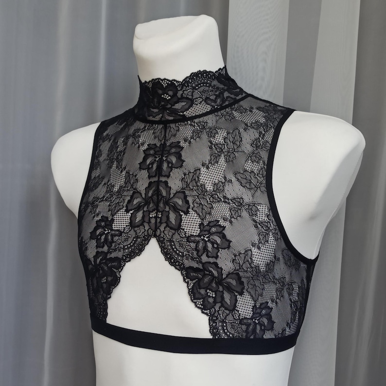 Pode incluir: Top preto de renda com al&ccedil;as, gola alta e um decote na frente. O top &eacute; feito de renda floral delicada.