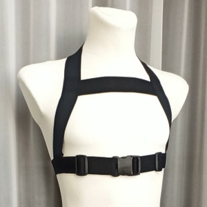 May include: A black adjustable harness with a buckle closure. The harness is made of a soft, comfortable material and is designed to fit snugly around the chest.