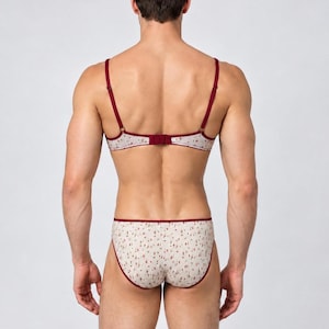 May include: A matching lingerie set consisting of a bra and briefs. The bra features thin adjustable straps and a back hook closure. Both pieces are made of a light-colored fabric with a small floral pattern and are trimmed in dark red.