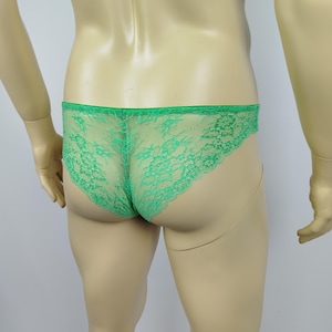 Puede incluir: Ropa interior de encaje verde brillante. La delicada tela es visible, con un borde festoneado a lo largo de la cintura y las aberturas de las piernas. La prenda se exhibe en un maniquí.