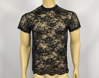 May include: A short-sleeved t-shirt made of black floral lace fabric. The garment features a solid black crew neckline and a scalloped hemline. The intricate lace pattern covers the entire front of the shirt, showcasing a detailed botanical design.