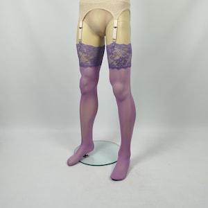 Pode incluir: Meias transparentes cor de lavanda até a coxa com faixas de renda floral larga e complexa num tom violeta a condizer. As meias estão presas a um cinto de ligas bege com alças ajustáveis e clipes metálicos num manequim.