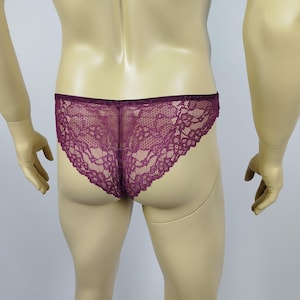 Puede incluir: Ropa interior de encaje color ciruela. El delicado patrón floral de encaje cubre la parte delantera y trasera de la braga. La ropa interior se exhibe en un maniquí.