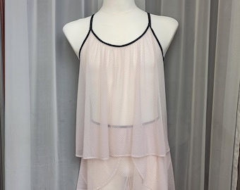 May include: A delicate pink and black mesh slip with a tiered skirt. The slip has a black trim around the neckline and straps.