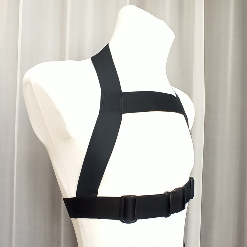 May include: Black adjustable chest harness with a buckle closure. The harness is made of a thick, durable material and has a simple design.