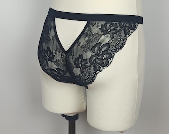 May include: Black lace underwear with a floral pattern. The underwear features a cut-out design in the back and a black waistband. The delicate lace creates a see-through effect.