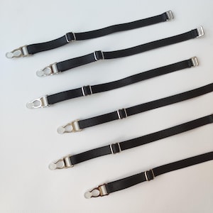 Puede incluir: Seis correas elásticas negras con clips metálicos plateados. Las correas son de diferentes longitudes.