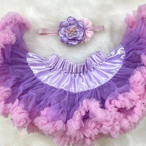 May include: A purple and pink tulle tutu skirt with a satin waistband and a matching flower headband with a butterfly embellishment.