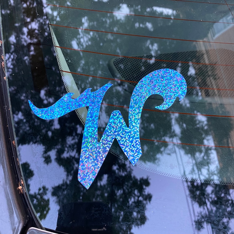 May include: A blue glitter decal of the letter "W" with a decorative flourish. The decal is on a car window.