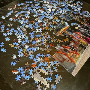 May include: A partially completed jigsaw puzzle on a wooden table. The puzzle features a colorful image of a building with an exit sign and the word "EXIT" printed on it. The puzzle pieces are scattered around the table, with some pieces already in place.