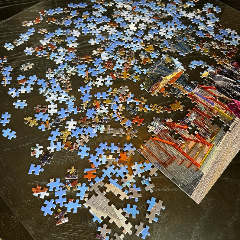 May include: A partially completed jigsaw puzzle on a wooden table. The puzzle features a colorful image of a building with an exit sign and the word "EXIT" printed on it. The puzzle pieces are scattered around the table, with some pieces already in place.
