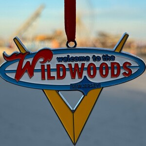 May include: A blue and yellow metal ornament shaped like a surfboard with the words "Welcome to the Wildwoods, New Jersey" in red and white lettering.