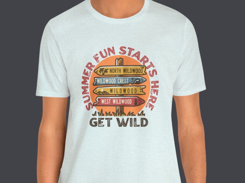 Pu&ograve; includere: Una maglietta grigio chiaro con una grafica circolare che recita "SUMMER FUN STARTS HERE" attorno a un design di palo segnaletico. Il palo segnaletico indica "NORTH WILDWOOD", "WILDWOOD CREST", "WILDWOOD" e "WEST WILDWOOD". Il testo "GET WILD" &egrave; sotto.