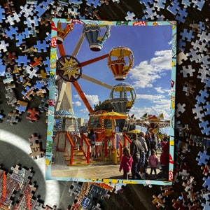 May include: A colorful carnival ride with a Ferris wheel, a carousel, and a swing ride. The ride is decorated with bright colors and lights. The ride is set against a blue sky with white clouds.