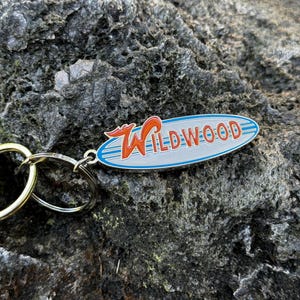 May include: A silver keychain with a blue and white oval charm that says "WILDWOOD" in red letters. The charm has a red and orange wave design.